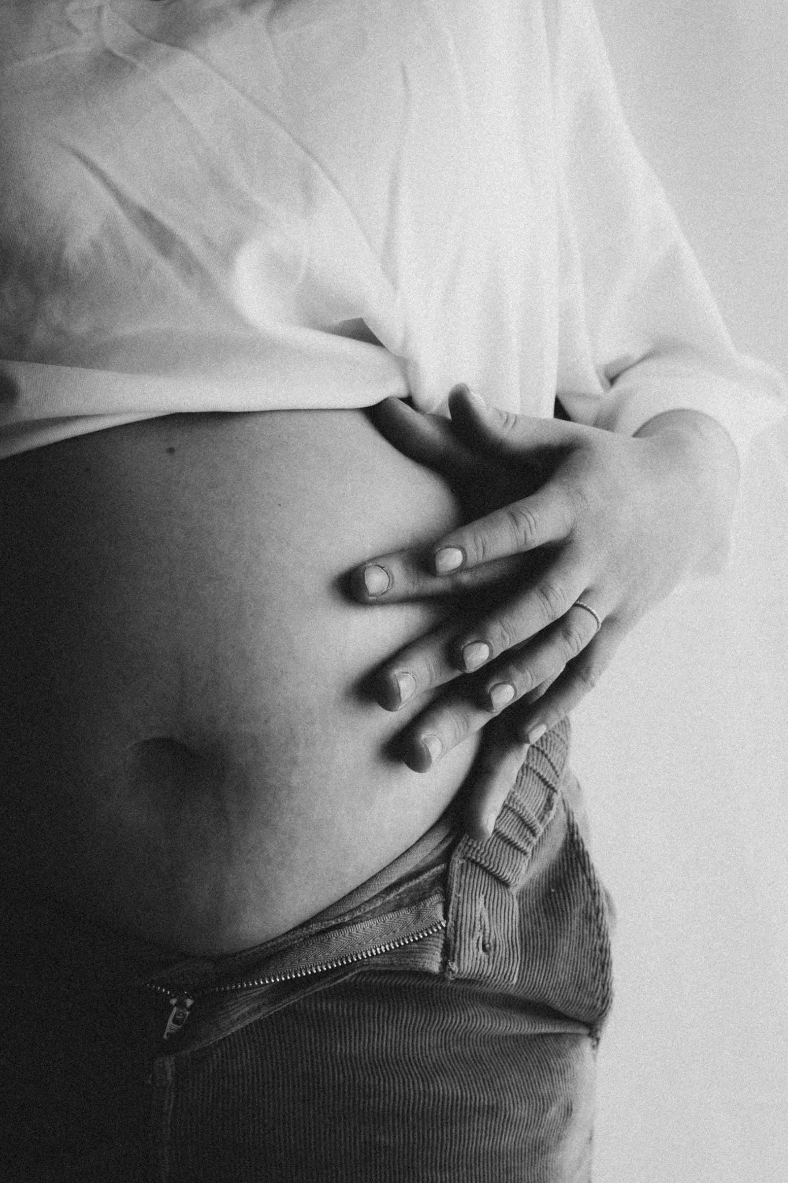 Schwarz-weiß-Nahaufnahme eines Babybauchs, eine Hand liegt darauf