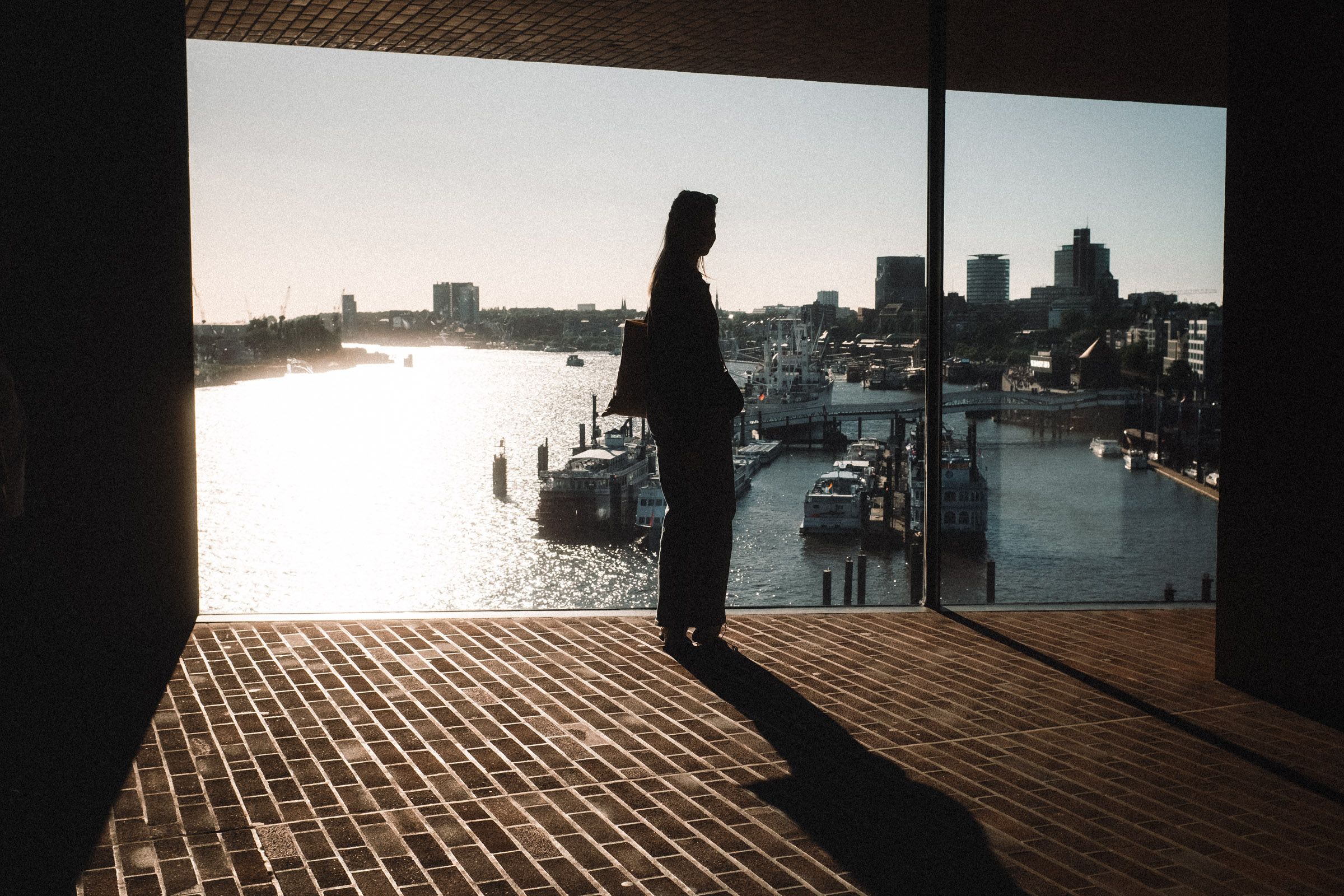 Silhouette einer Person vor einem großen Fenster mit Blick auf den Hafen