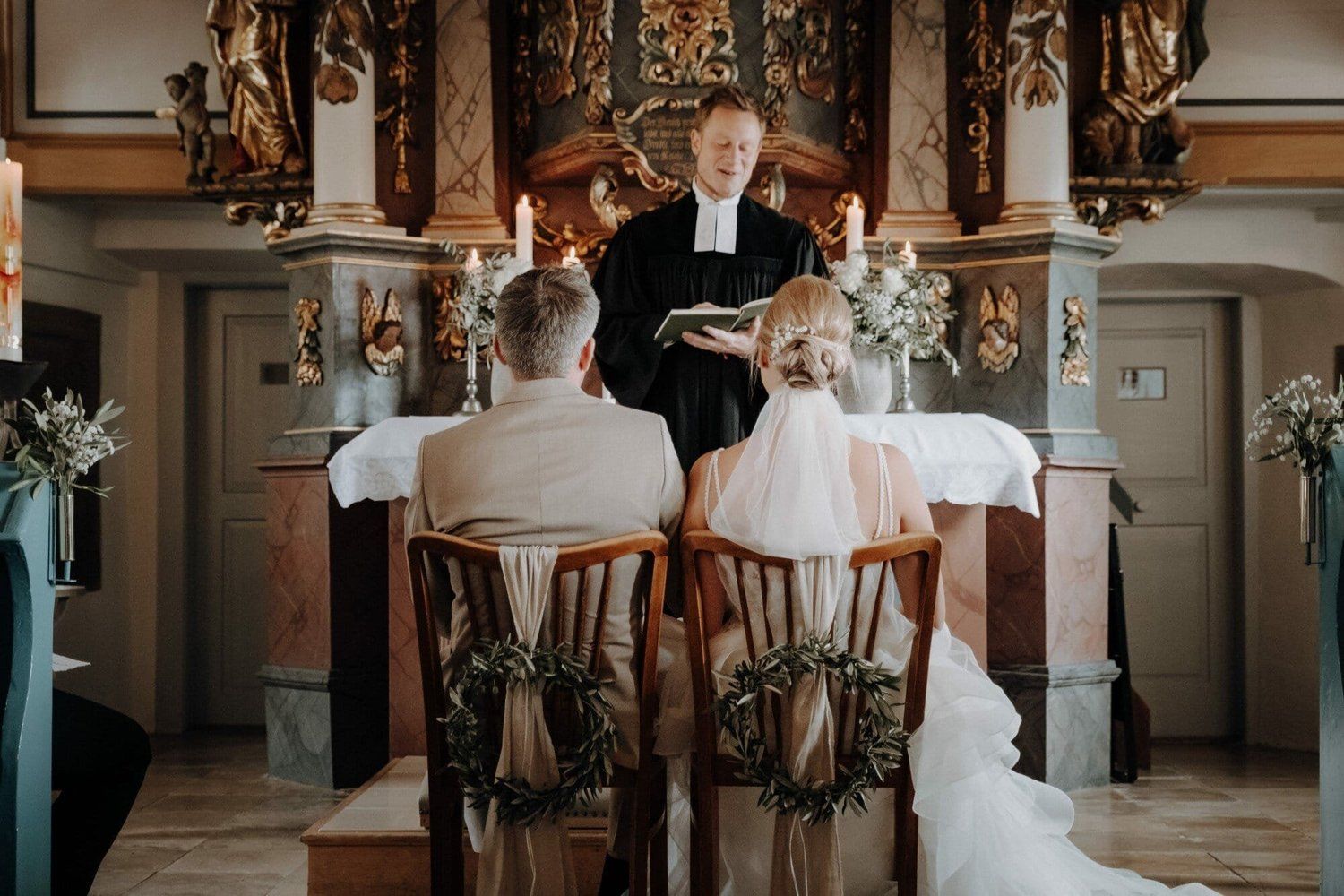 Brautpaar sitzt vor dem Altar einer festlich geschmückten Kirche mit Kerzenlicht